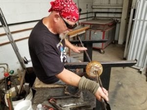 Glass Blower in the bench opening a bowl with tool